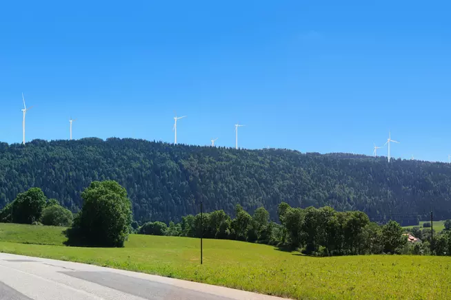 Blick auf eine hügelige Landschaft mit Windrädern und klarem blauem Himmel.