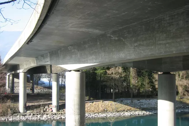 Betonbrücke über einen ruhigen Fluss, Stützpfeiler sichtbar.