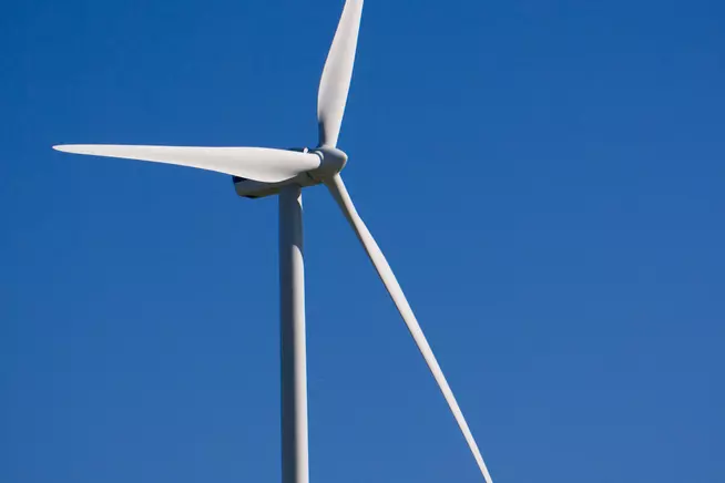 Windkraftanlage auf einer grünen Wiese vor blauem Himmel.