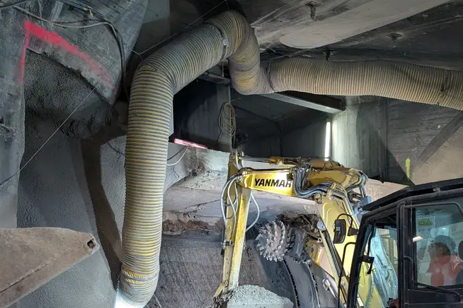 Bauausrüstung in einem Tunnel mit grossen Rohren und einem Bagger.