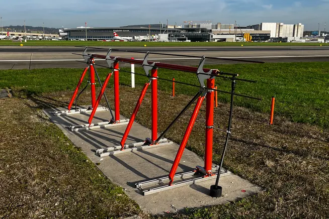 Rote Fahrradständer stehen auf einem Betonfundament neben einem Flughafen.