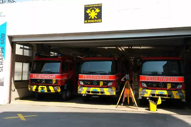 Drei rote Feuerwehrfahrzeuge stehen in einer Fahrzeughalle.
