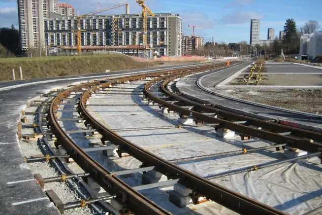 Kurve von Gleisen mit Baustellen im Hintergrund und klarem, blauem Himmel.